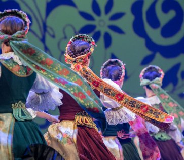 Mazowsze Ensemble dancers on stage in costumes from Rozbark, with decorative ribbons attached to their headdresses