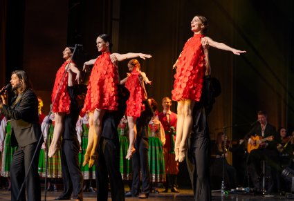 Tancerze ubrani na czarno podnoszący tancerki w czerwonych sukienkach podczas układu, obok widoczny wokalista zespołu Pectus, a w tle orkiestra