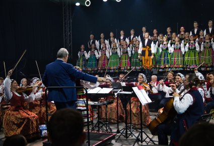 Solista Chóru wykonujący utwór Furman, za nim pozostała część Artystów Chóru w kostiumach łowickich, niżej Artyści Orkiestry w kostiumach wilanowskich wraz z Dyrygentem