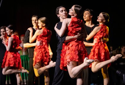 Tancerze ubrani na czarno przytulający tancerki w czerwonych sukienkach podczas układu