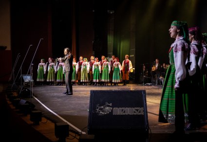 Wokalista zespołu Pectus na scenie wraz z chórem w kostiumach kurpiowskich