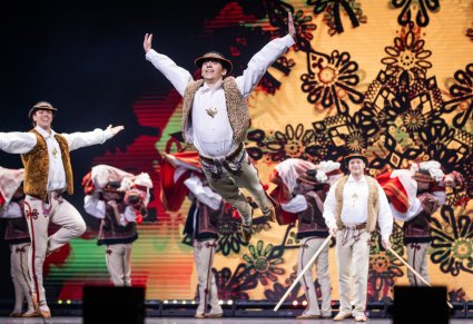 Zbliżenie na tancerza w kostiumie jurgowskim w akrobacji tanecznej, w tle widoczna grupa tancerzy