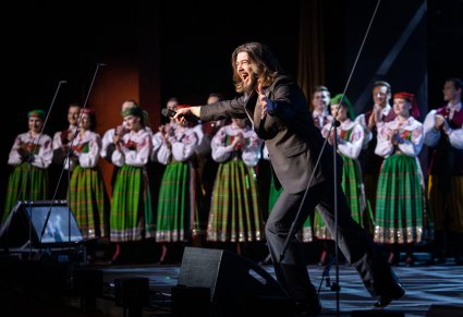 Wokalista zespołu Pectus na scenie wraz z chórem w kostiumach kurpiowskich