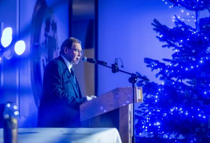 Przemawiająca osoba przed koncertem, w tle choinka