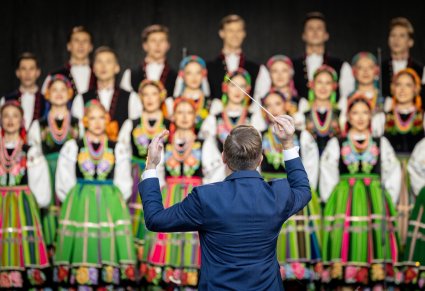 Dyrygent na tle chóru w kostiumach łowickich
