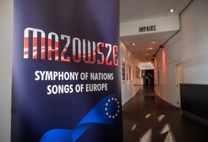 Materiał marketingowy na pierwszym planie: napis MAZOWSZE SYMPHONY OF NATIONS SONGS OF EUROPE w tle korytarz prowadzący na miejsce koncertu