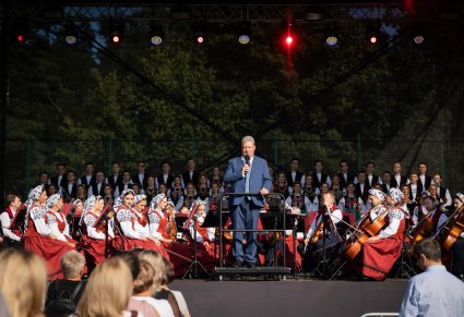 Dyrektor zespołu, przemawiający podczas koncertu, w tle chór i orkiestra