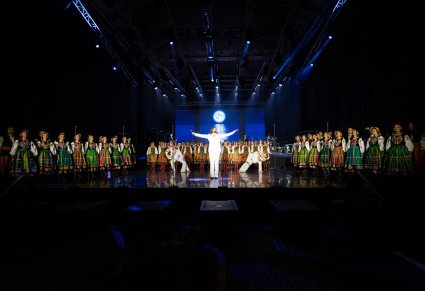 Na środku sceny wokalista zespołu Pectus wraz z Artystami Baletu w kostiumach współczesnych, wykonujący choreografię taneczną. Po bokach sceny jak i na tyłach widoczna grupa Artystów w kostiumach ludowych