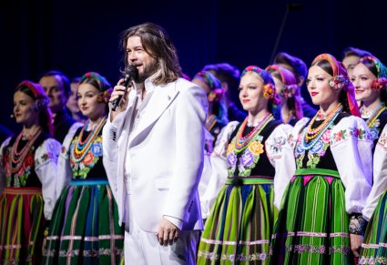 Wokalista zespołu Pectus na scenie wraz z chórem w kostiumach łowickich