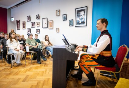 Artysta zespołu Mazowsze prowadzący warsztaty wokalne, w tle widoczne dzieci