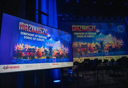 Chwile przed koncertem, wyświetlony na monitorach przy scenie plakat wydarzenia, na scenie ustawione miejsca dla Orkiestry