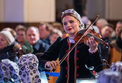 Na pierwszym planie Muzyczka z Orkiestry grająca na instrumencie smyczkowym