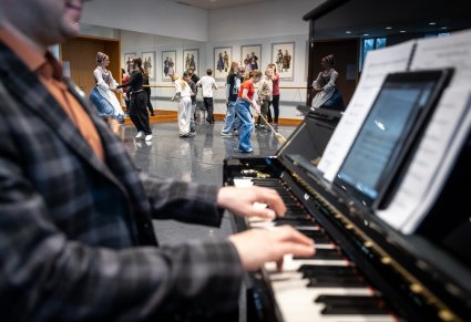 Zbliżenie na akompaniatora grającego na pianinie, w tle tańczące dzieci