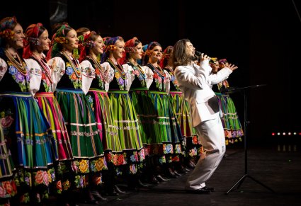 Wokalista zespołu Pectus na scenie wraz z chórem w kostiumach łowickich