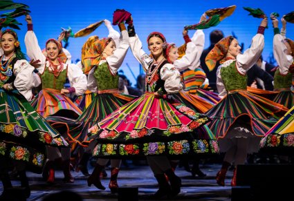 Zbliżenie na tancerkę w kostiumie łowickim w obrocie, w tle widoczne inne tancerki