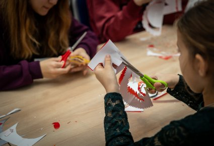 Zbliżenie na dziewczynkę robiącą wycinankę kurpiowską podczas warsztatów