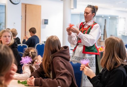 Artystka ludowa podczas warsztatów uczy dzieci robienia kwiatów z bibuły