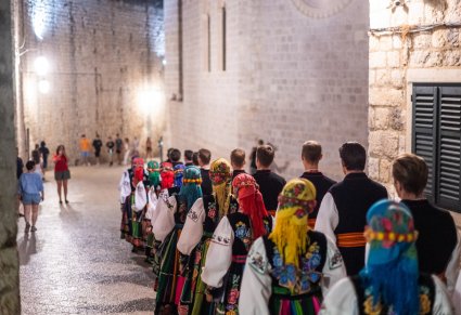 Artyści w parach w kostiumach łowickich w trakcie przemieszczania się do sali w której odbędzie się koncert