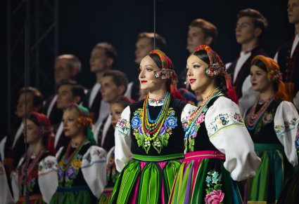 Zbliżenie na Solisty w kostiumach łowickich, za nimi pozostała część Artystów Chóru