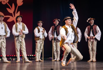 Tancerz w kostiumie jurgowskim w figurze tanecznej, w tle grupa tancerzy