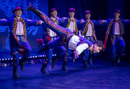 Tancerze w kostiumie podegrodzkim w akrobacji tanecznej, w tle widoczna grupa tancerzy