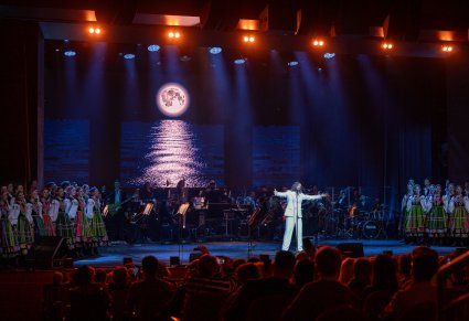 Wokalista zespołu Pectus na scenie wraz z chórem w kostiumach łowickich, w tle widoczna orkiestra z dyrygentem