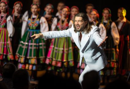 Wokalista zespołu Pectus na scenie, w tle chór w kostiumach łowickich