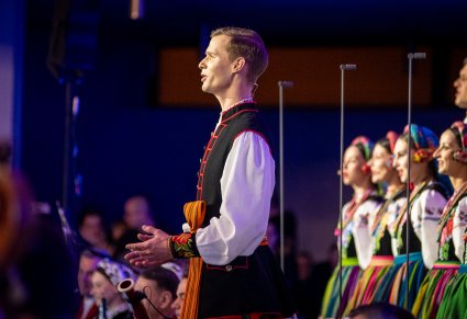 Zbliżenie na solistę chóru podczas koncertu z widocznych chórem w tle