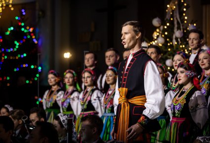 Na pierwszym planie Solista w trakcie śpiewu, za nim część Artystów Chóru w kostiumach łowickich