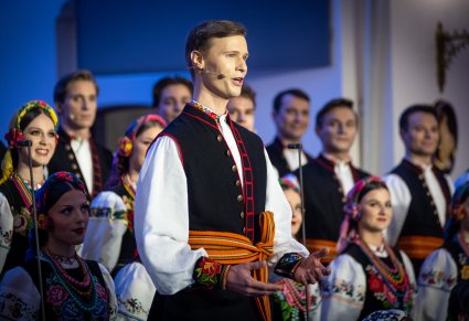 Zbliżenie na solistę chóru podczas koncertu z widocznych chórem w tle