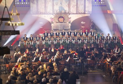 Artyści Chóru w kostiumach łowickich w trakcie śpiewu, niżej Artyści Orkiestry w kostiumach wilanowskich wraz z Dyrygentem