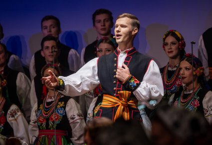 Zbliżenie na solistę chóru podczas koncertu z widocznych chórem w tle