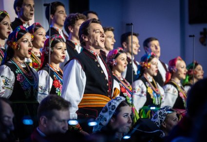 Zbliżenie na solistę chóru podczas koncertu z widocznych chórem w tle