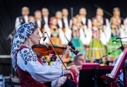 Zbliżenie na skrzypaczkę w kostiumie wilanowskim, w tle chór w kostiumach łowickich