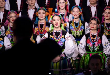 Na pierwszym planie śpiewająca Solistka, za nią część Artystów Chóru w kostiumach łowickich