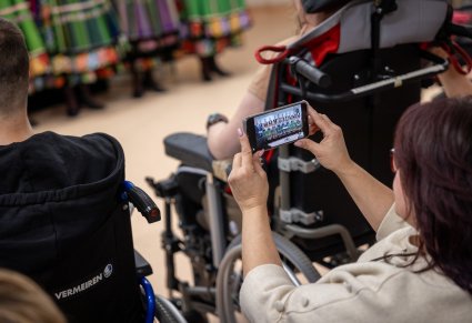 Na pierwszym planie widać telefon nagrywający Artystów Chóru w kostiumach łowickich wraz z Dyrektorem zespołu "Mazowsze"