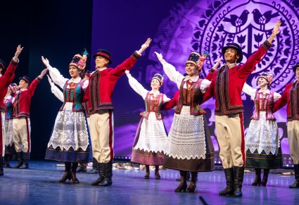 Artyści w kostiumach kurpiowskich podczas wykonywania choreografii tanecznej na scenie