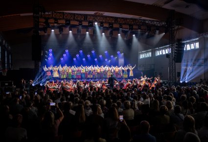 Na scenie Artyści w kostiumach opoczyńskich w trakcie wykonywania choreografii tanecznej, niżej Orkiestra w kostiumach wilanowskich wraz z Dyrygentem i widoczna część Publiczności