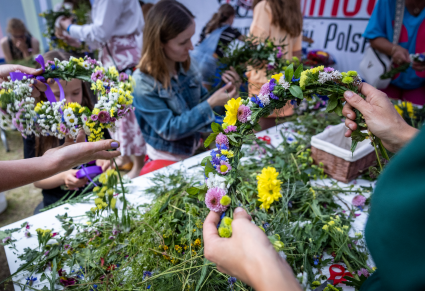 Uczestnicy warsztatów wiją wianki ze świeżych kwiatów w namiocie warsztatowym Centrum Folkloru Polskiego