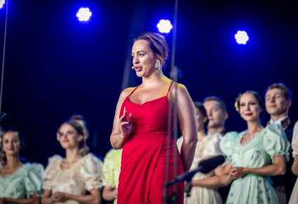 Solistka w długiej, czerwonej sukience a za nią Artyści w kostiumach stylowych koniec XIX w.