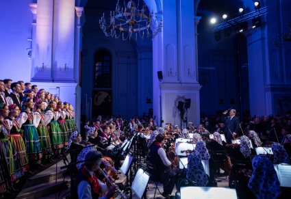 Widok na Artystów Chóru w kostiumach łowickich, Dyrygenta zwróconego w stronę Orkiestry w kostiumach wilanowskich