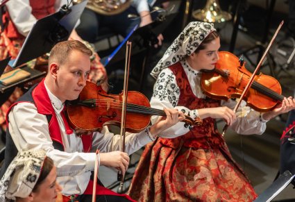 Zbliżenie na artystów orkiestry grających na instrumentach smyczkowcyh