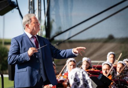 Zbliżenie na Dyrektor zespołu, w trakcie dyrygowania, w tle fragment orkiestry