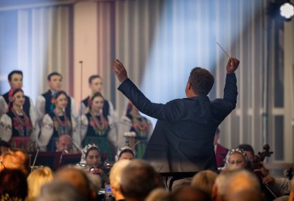 Dyrygent z batutą, zwrócony w stronę Orkiestry i Chóru
