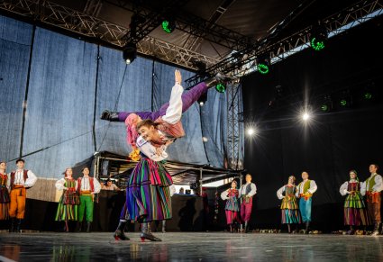 Na środku sceny para Artystów Baletu w kostiumach opoczyńskich wykonująca spektakularną choreografię taneczną, po bokach sceny reszta część Artystów