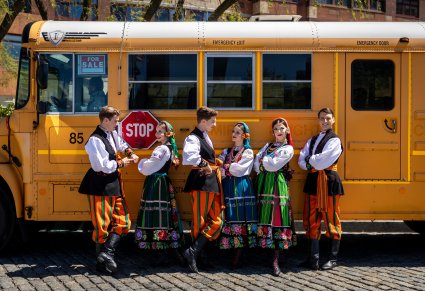 3 Pary Artystów w kostiumach łowickich przed charakterystycznym pomarańczowym autobusem szkolnym w Nowym Jorku