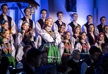 Zbliżenie na solistkę chóru podczas koncertu z widocznych chórem w tle