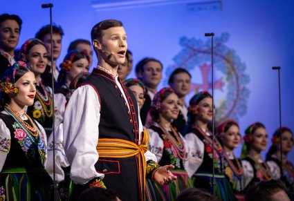 Na pierwszym planie Solista a w tle Artyści Chóru w kostiumach łowickich