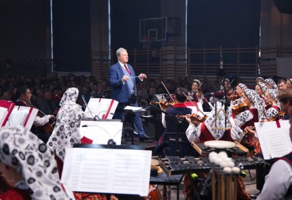 Widok na Dyrygenta zwróconego w stronę Artystów Orkiestry, trzymającego w ręku batutę. Orkiestra w kostiumach wilanowskich