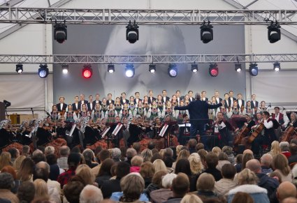 Chór w kostiumach łowickich, orkiestra w kostiumach wilanowskich wraz z dyrygującycm Dyrektorem zespołu, podczas koncertu na scenie - daleki widok z zza publiczności